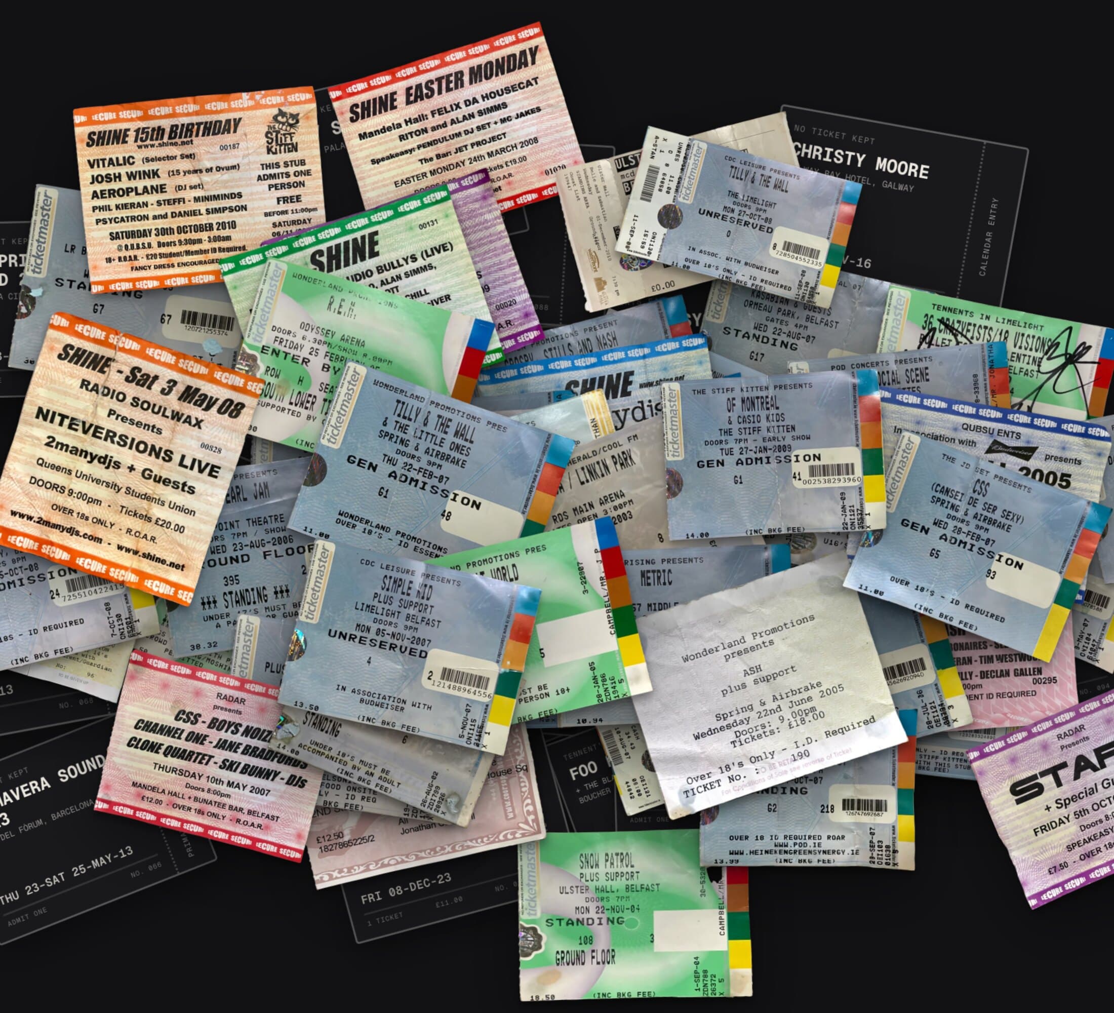 Gig tickets heaped on a dark table: Shine club-night tickets in orange and cream, pale blue and green Ticketmaster tickets with colour bars down their stubs, Ash at Spring & Airbrake on white paper, and among them dark outlined tickets for gigs with no paper left, like Christy Moore and Primavera Sound 2013.